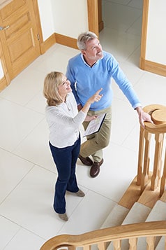 a couple standing in a house while both looking upstairis